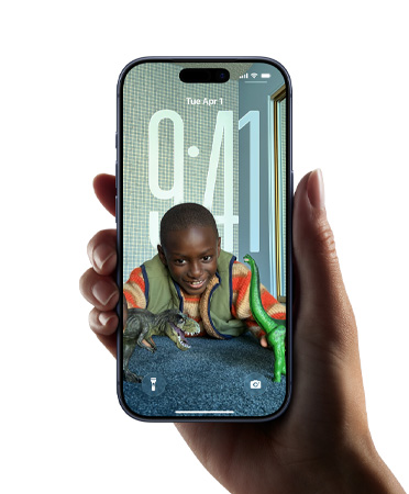 Na iPhonu, který někdo drží v ruce, je vidět nový Liquid Glass design, ve kterém se hodiny dynamicky přizpůsobují obrázku na zamknuté obrazovce